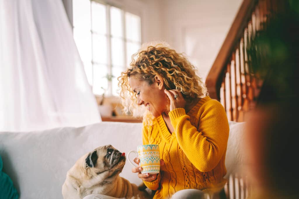 Adult female relaxes on a comfortable sofa at home while engaging with her beloved pug to share genuine comfort and unwavering support, reinforcing daily well-being and emotional balance throughout
