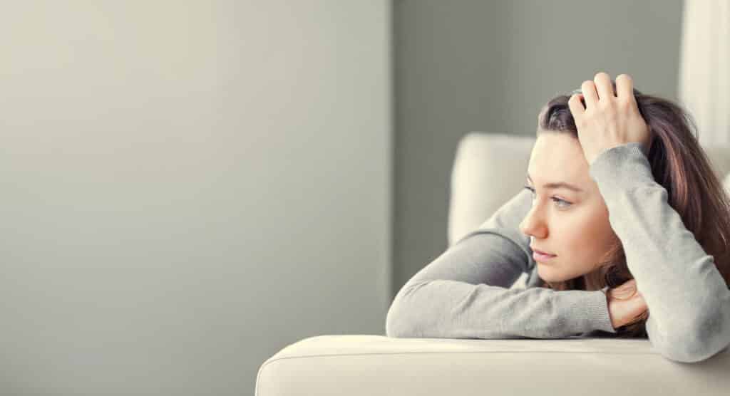 Young woman lying at home in living room sitting on sofa. She feeling sad and worried suffering depression in mental health. Problems and broken heart concept.