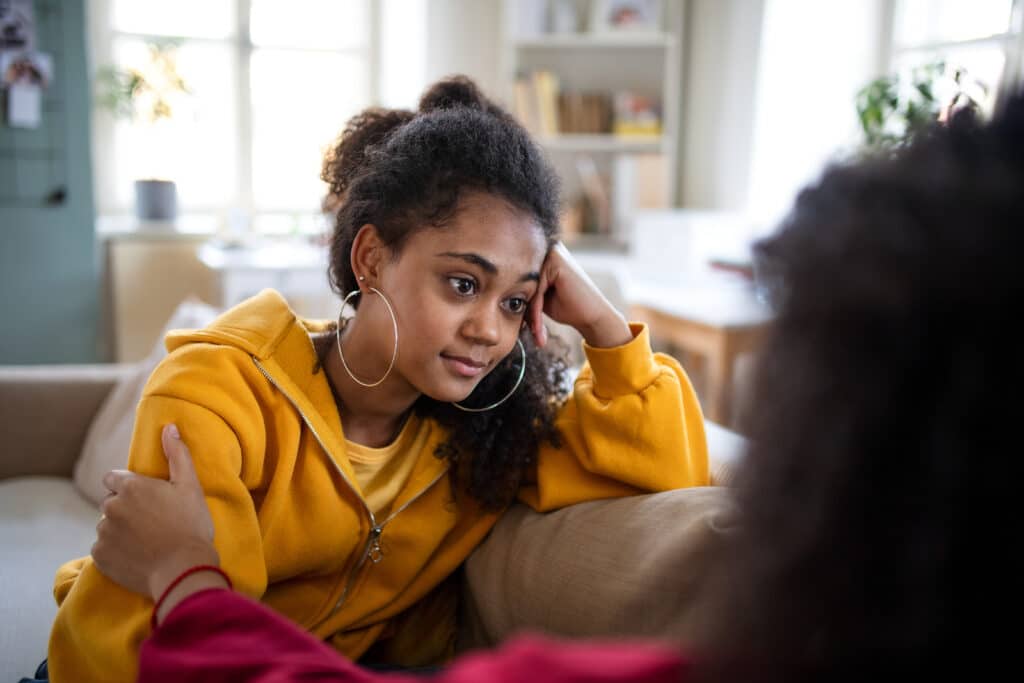 Portrait of sad teenager indoors at home, talking to parent.