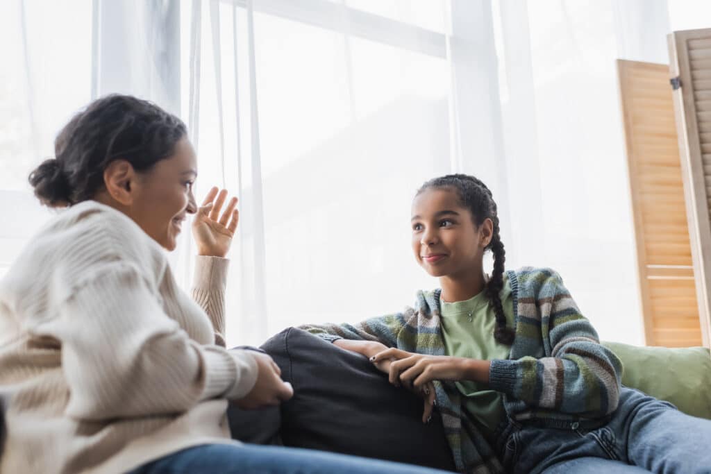 african american woman gesturing while talking to smiling teenage daughter
