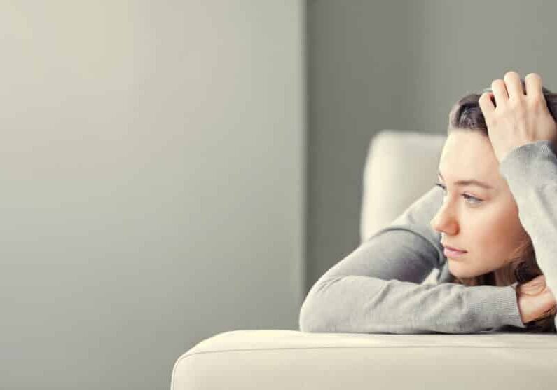 Young woman lying at home in living room sitting on sofa. She feeling sad and worried suffering depression in mental health. Problems and broken heart concept.