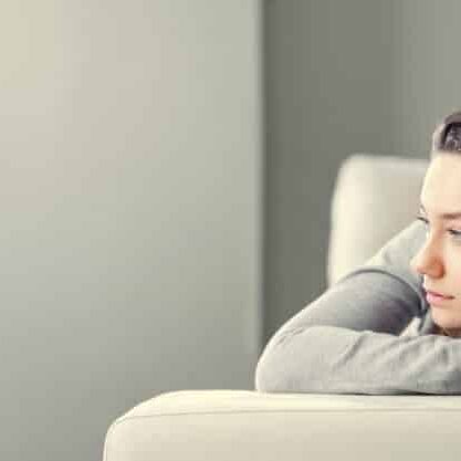 Young woman lying at home in living room sitting on sofa. She feeling sad and worried suffering depression in mental health. Problems and broken heart concept.