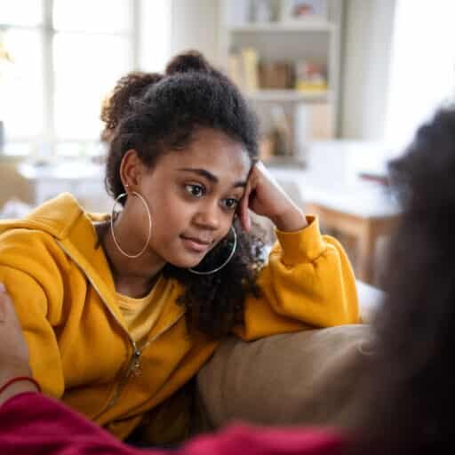 Portrait of sad teenager indoors at home, talking to parent.