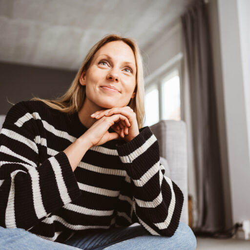 Woman in her 30s Sitting on the Floor in Front of Sofa and Smiling at Something Off-Camera; anxiety recovery stories