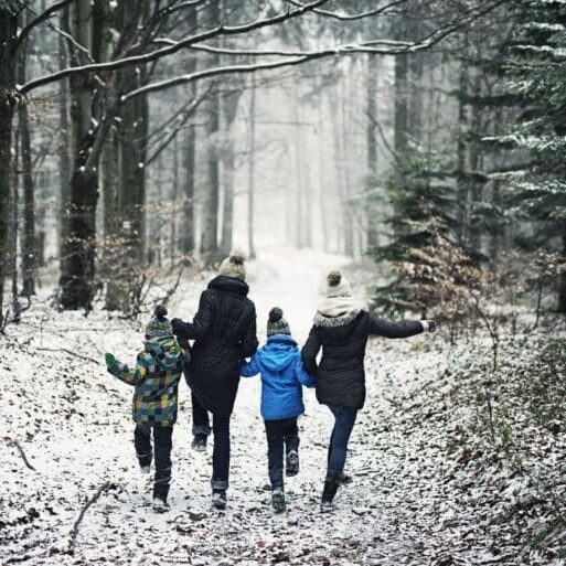 Mother with three kids running in beautiful winter forest. The little girl is aged 10 and her brothers are aged 7. Cold winter day