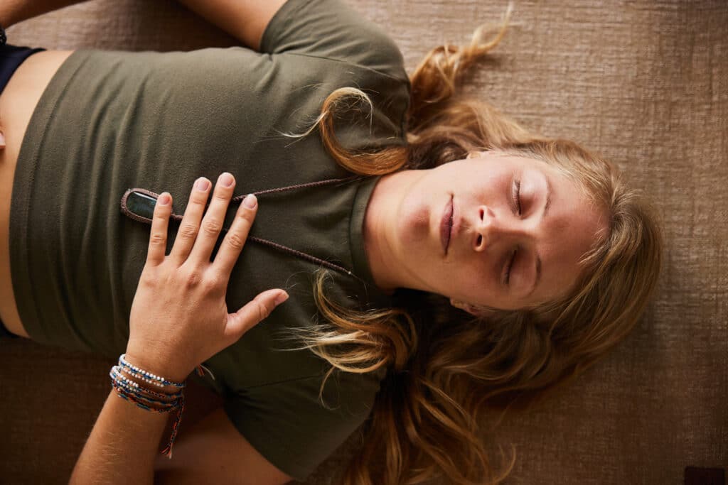 Young woman in sportswear doing breathing exercises while lying on an exercise mat on the floor of a studio during a yoga class