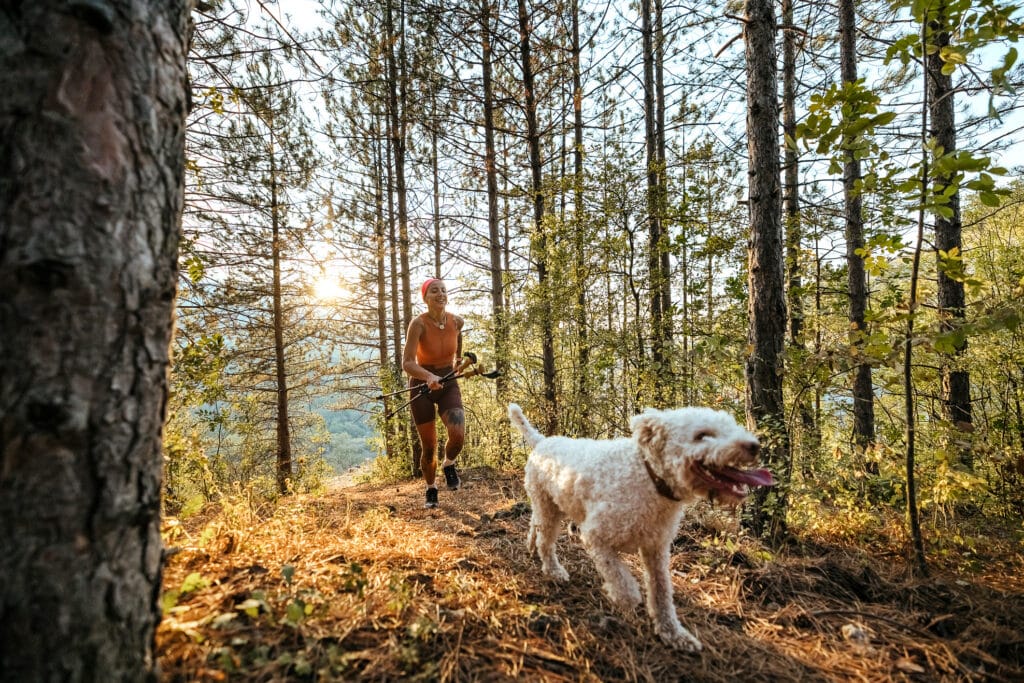 Shot of a young woman running in the forest with her  dog.