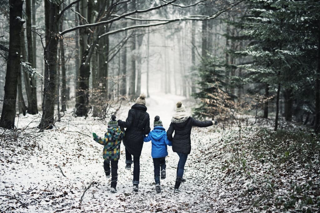 Mother with three kids running in beautiful winter forest. The little girl is aged 10 and her brothers are aged 7. Cold winter day